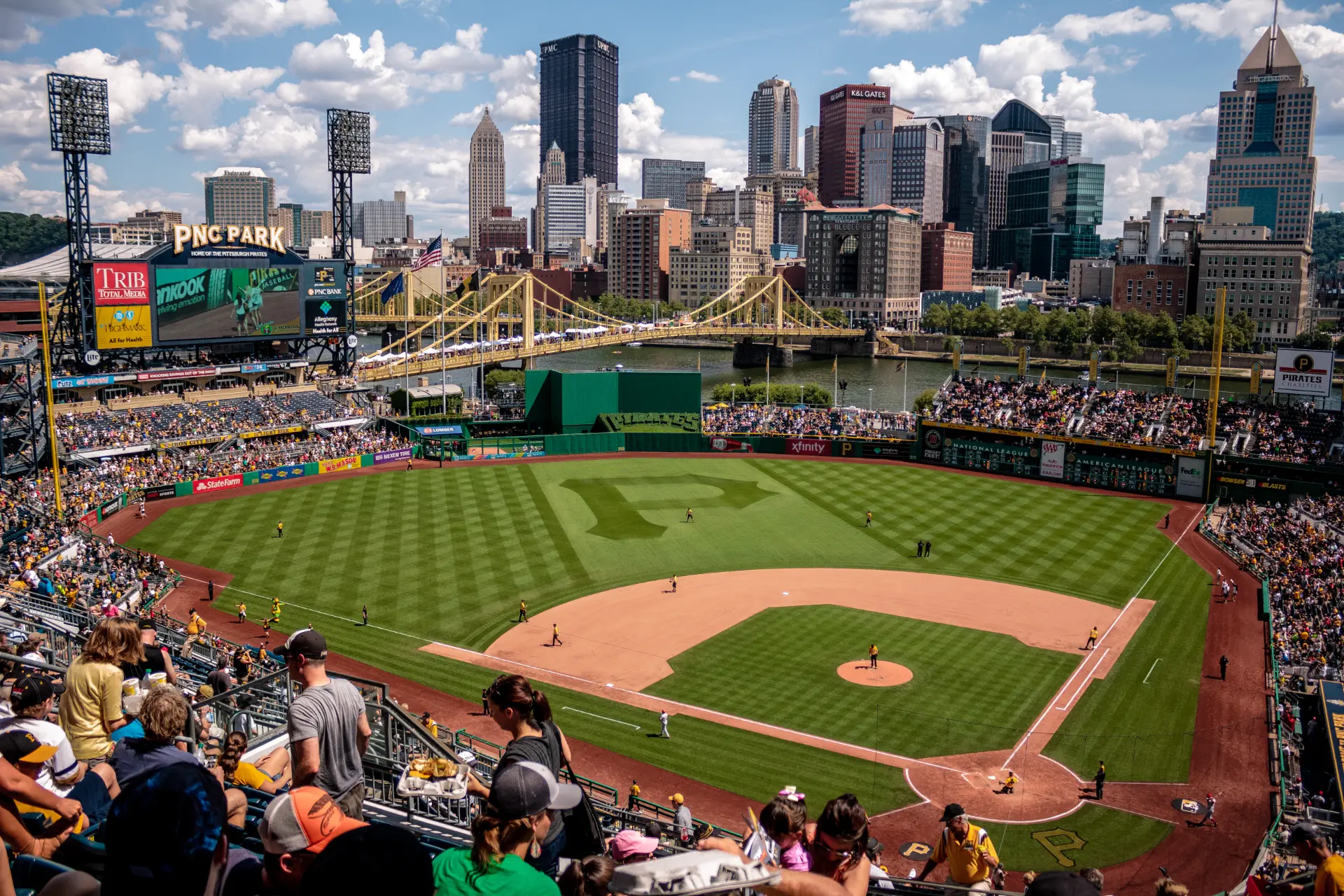 PNC Park during a Pirates game with the Downtown Pittsburgh skyline and yellow bridges behind the outfield